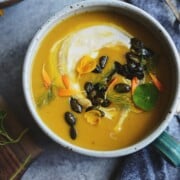 Vegan buttercup squash soup topped with coconut milk, maple spiced pumpkin seeds, edible flower petals and herbs in a bowl.