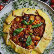 Rustic vegan tomato tart with pastry crust and sliced heirloom tomato filling garnished with fresh basil leaves on a serving plate with fresh thyme sprigs.