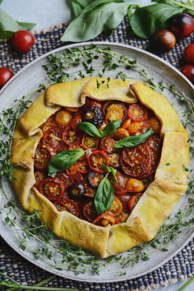 Rustic vegan tomato tart with pastry crust and sliced heirloom tomato filling garnished with fresh basil leaves on a serving plate with fresh thyme sprigs.