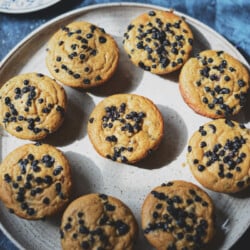 Top down view of vegan wild huckleberry muffins on a white ceramic plate and blue background.