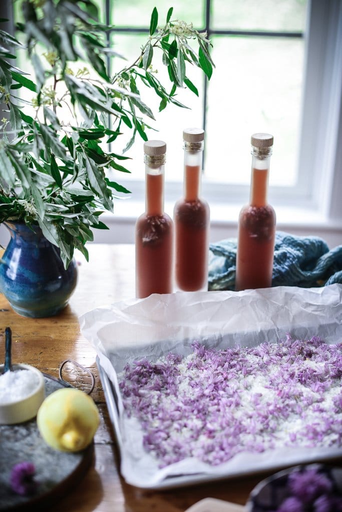 chive blossom vinegar in bottles on a table with a tray of chive blossom finishing salt in the foreground