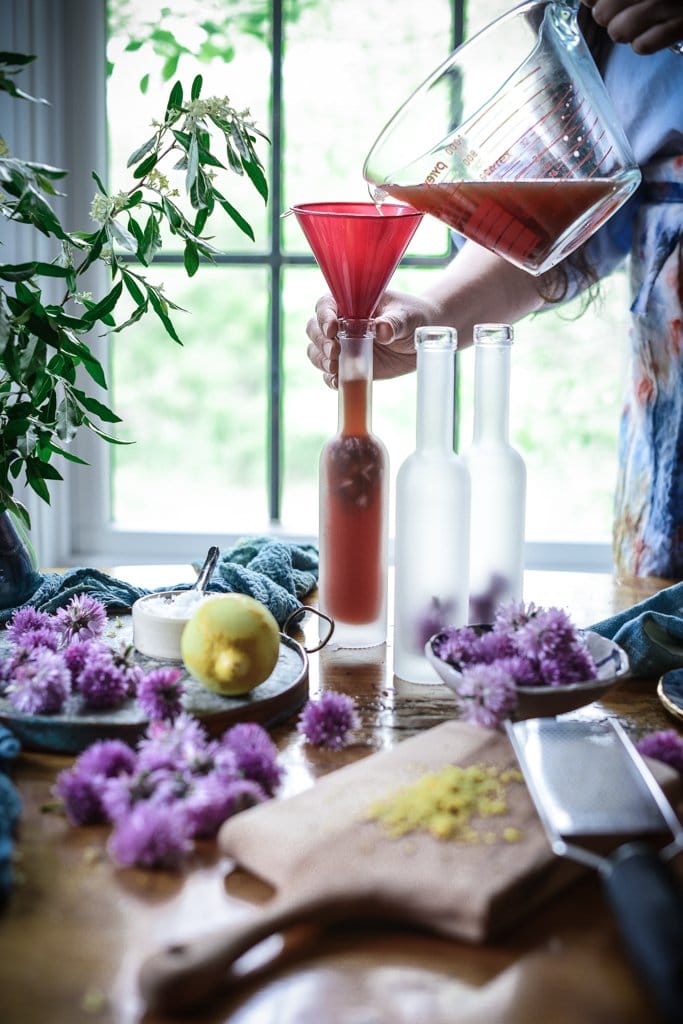 vinegar is being poured into a bottle with chive flowers