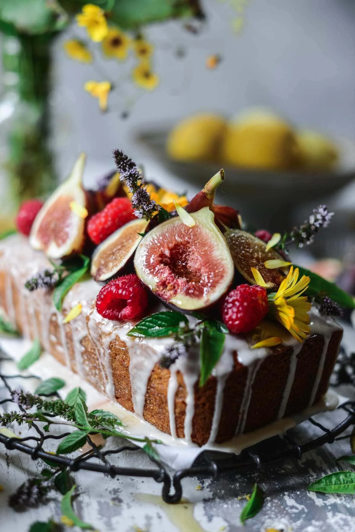 olive oil honey cake with lemon glaze and topped with fresh berries, figs, edible flowers and herbs