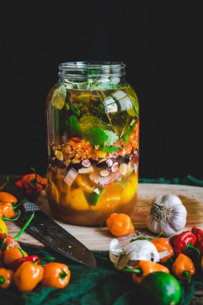 Large gallon-size glass mason jar of fire cider in the infusion stage with raw apple cider vinegar and medicinal plant materials.
