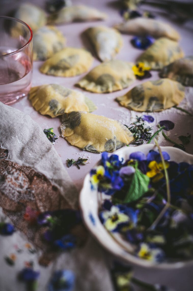 Shaped edible flower laminated pierogi sit on a table before they are cooked.