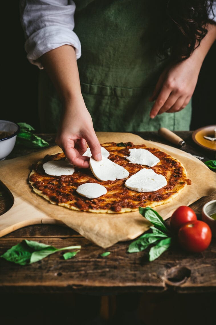 Kaity arranges slices of fresh mozzarella cheese on top of the uncooked gluten free pizza.