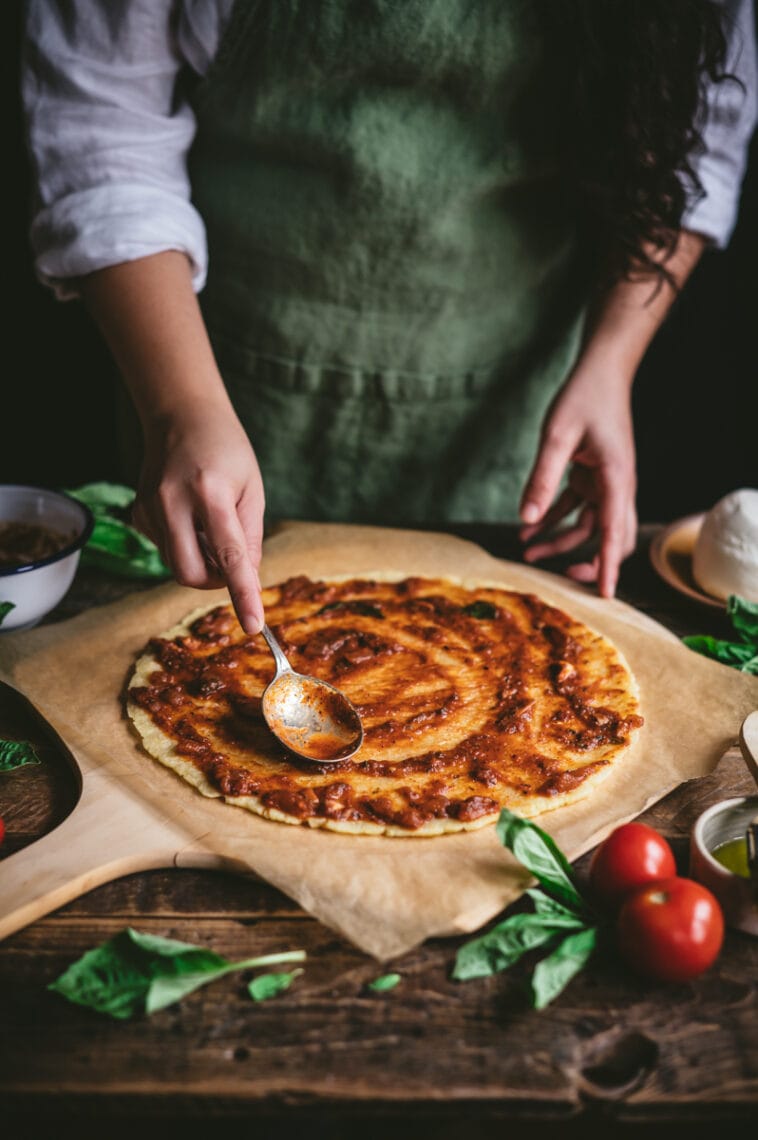 Kaity spoons tomato sauce onto gluten-free cassava-chickpea pizza dough.
