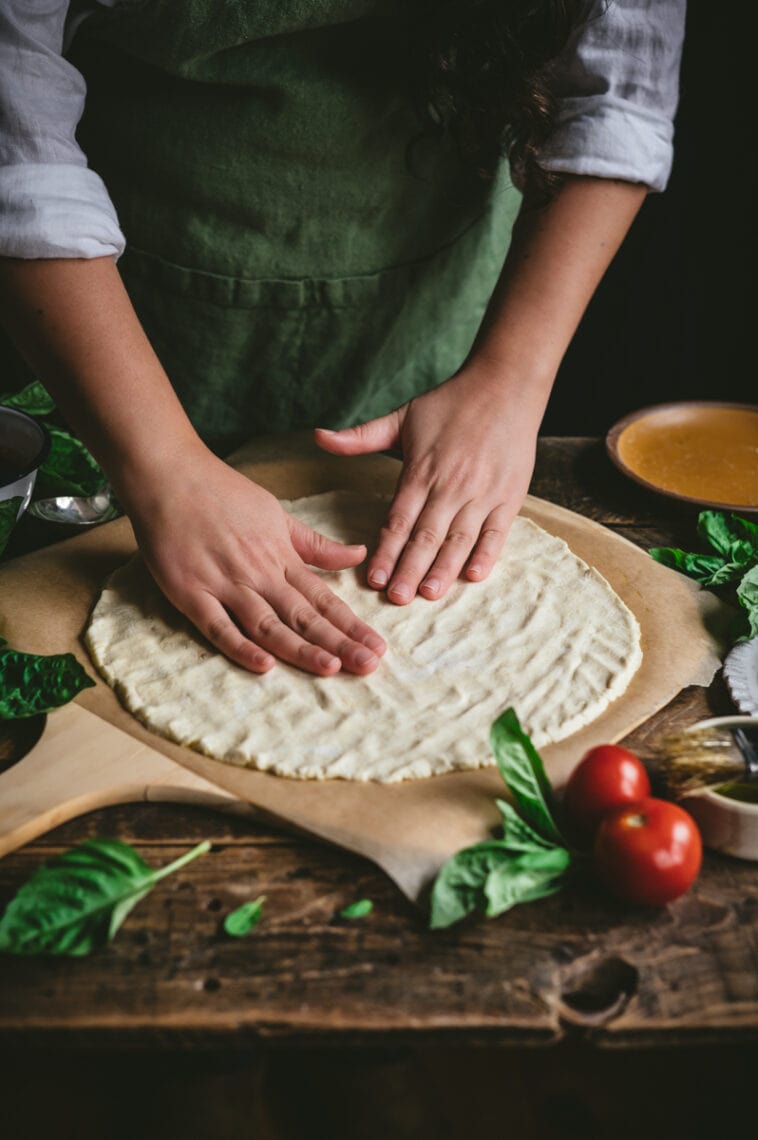 Kaity forms gluten-free cassava-chickpea pizza dough nto a pizza crust on top of a parchmnet paper lined pizza peel..