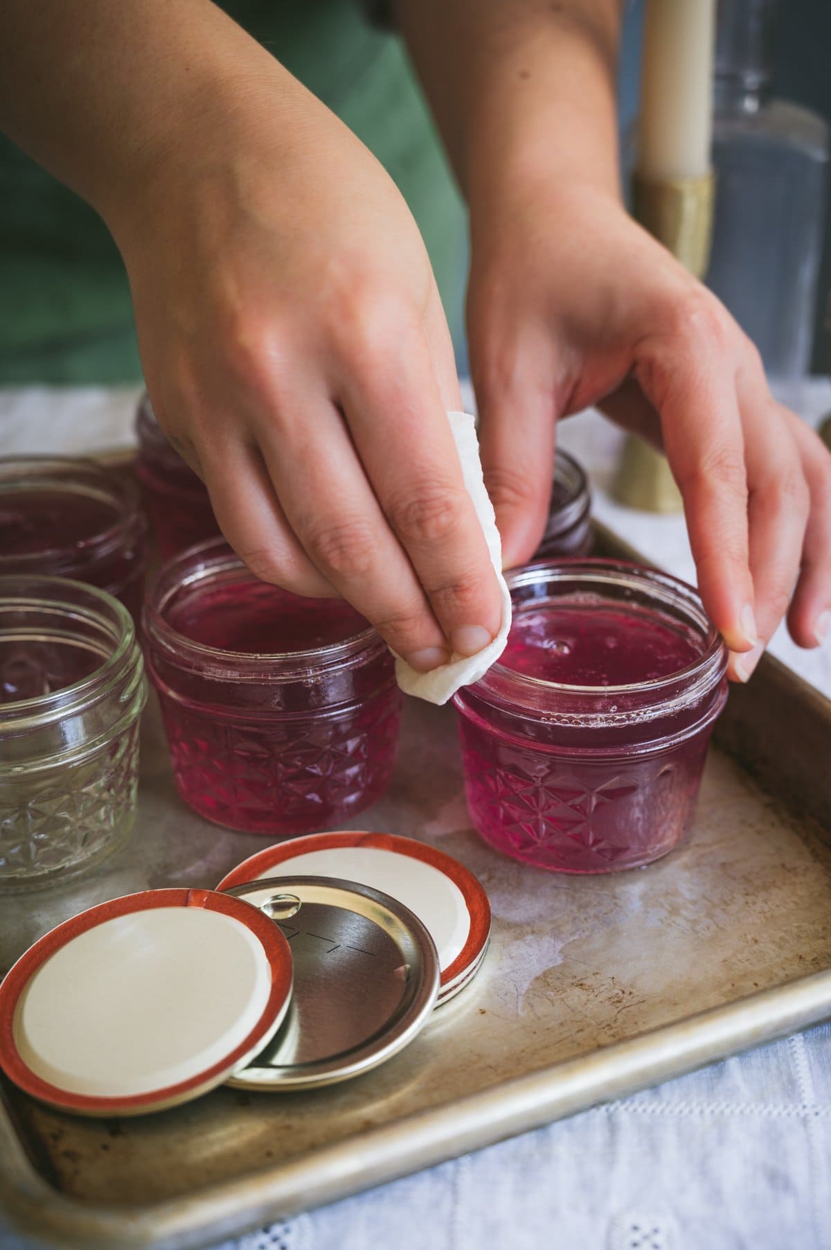 Kaity wipes the rims of filled jars of violet jelly with a damp cloth.