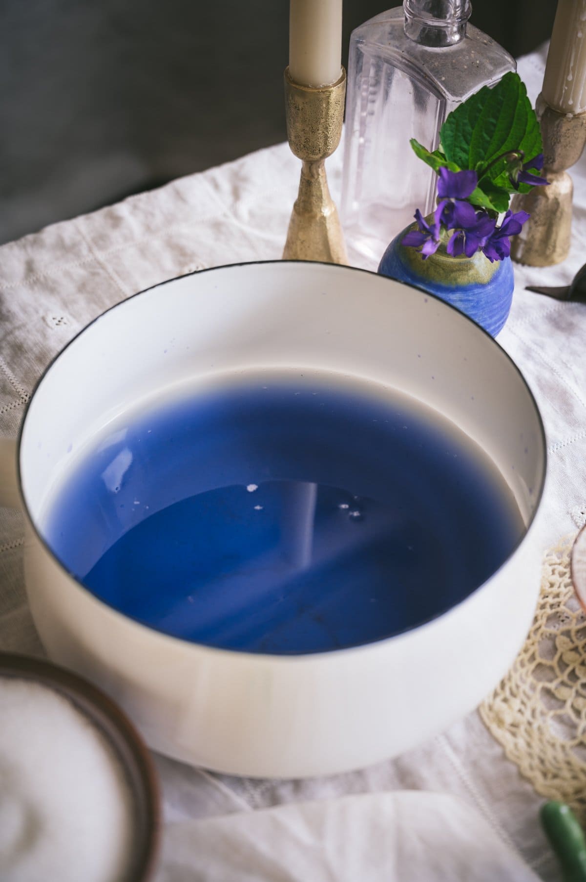 Angled closeup shot of a white enamel sacuepan holding the strained blue violet infusion.