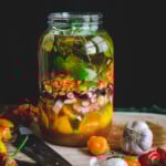 Large gallon-size glass mason jar of fire cider in the infusion stage with raw apple cider vinegar and medicinal plant materials.
