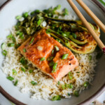 Teriyaki ginger miso glazed salmon and charred boy choy with scallions over a bed of white rice in a bowl.