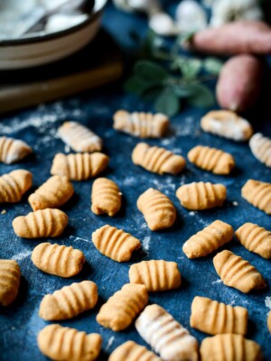 Uncooked vegan 3-ingredient sweet potato gnocchi shaped by hand on a blue background.