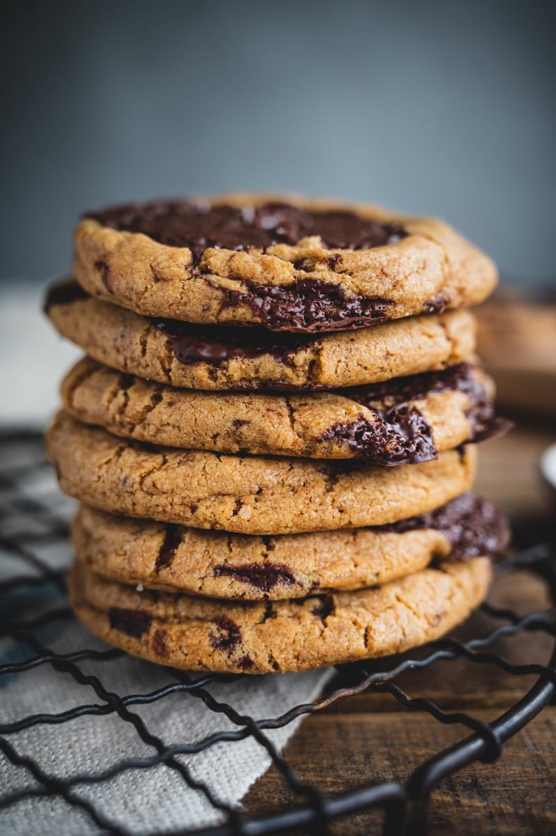 A close-up of a stack of six whole wheat chocolate chip cookies resting on a metal cooling rack, with gooey chocolate chunks visible in the cookies.