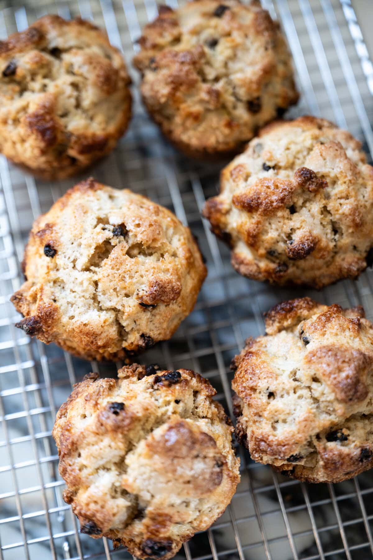 Six golden-brown, rustic Irish soda bread scones with a crumbly texture and visible currants resting on a metal cooling rack.
