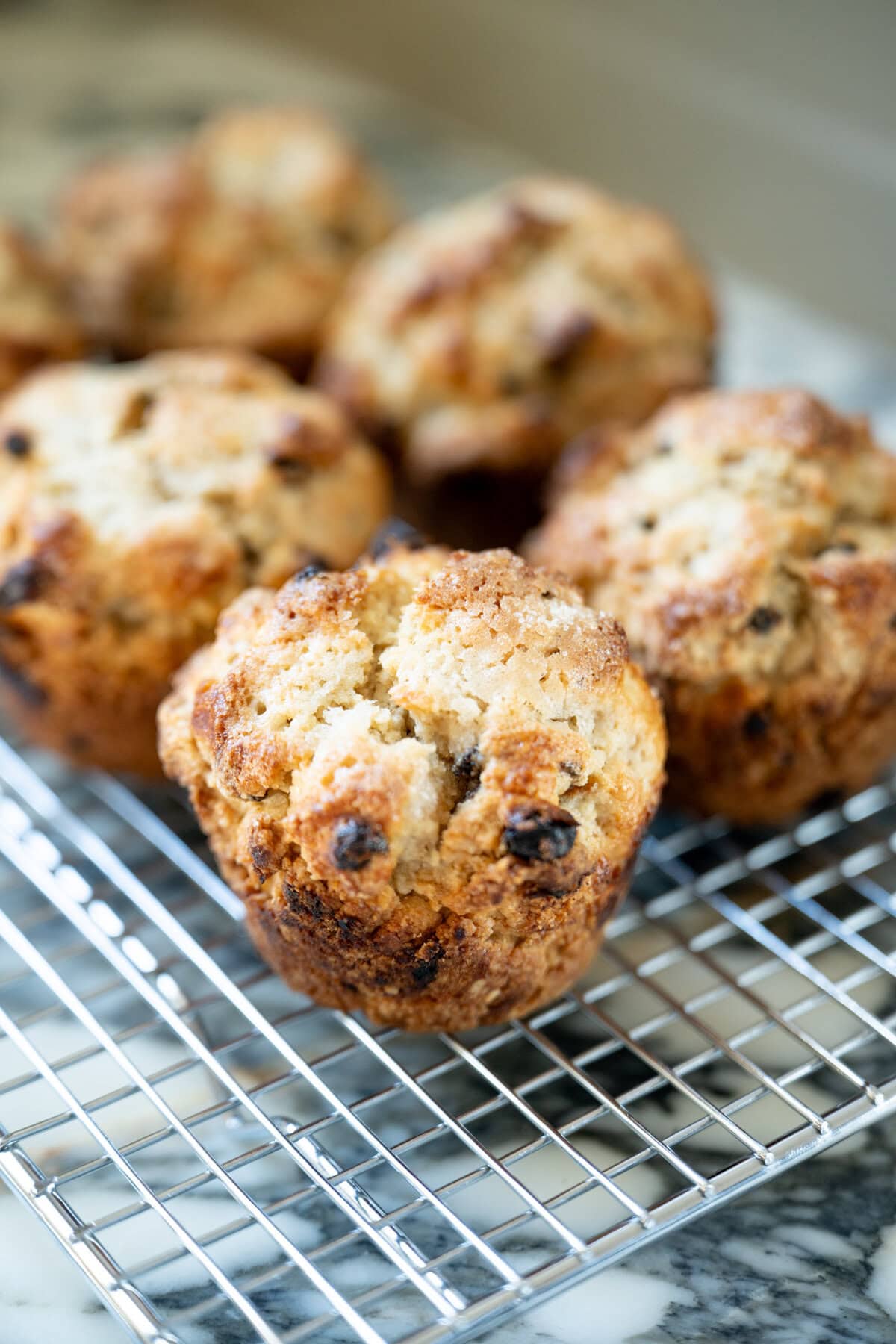 Freshly baked Irish soda bread scones with currants cooling on a wire rack, a marble countertop underneath and more scones blurred in the background.