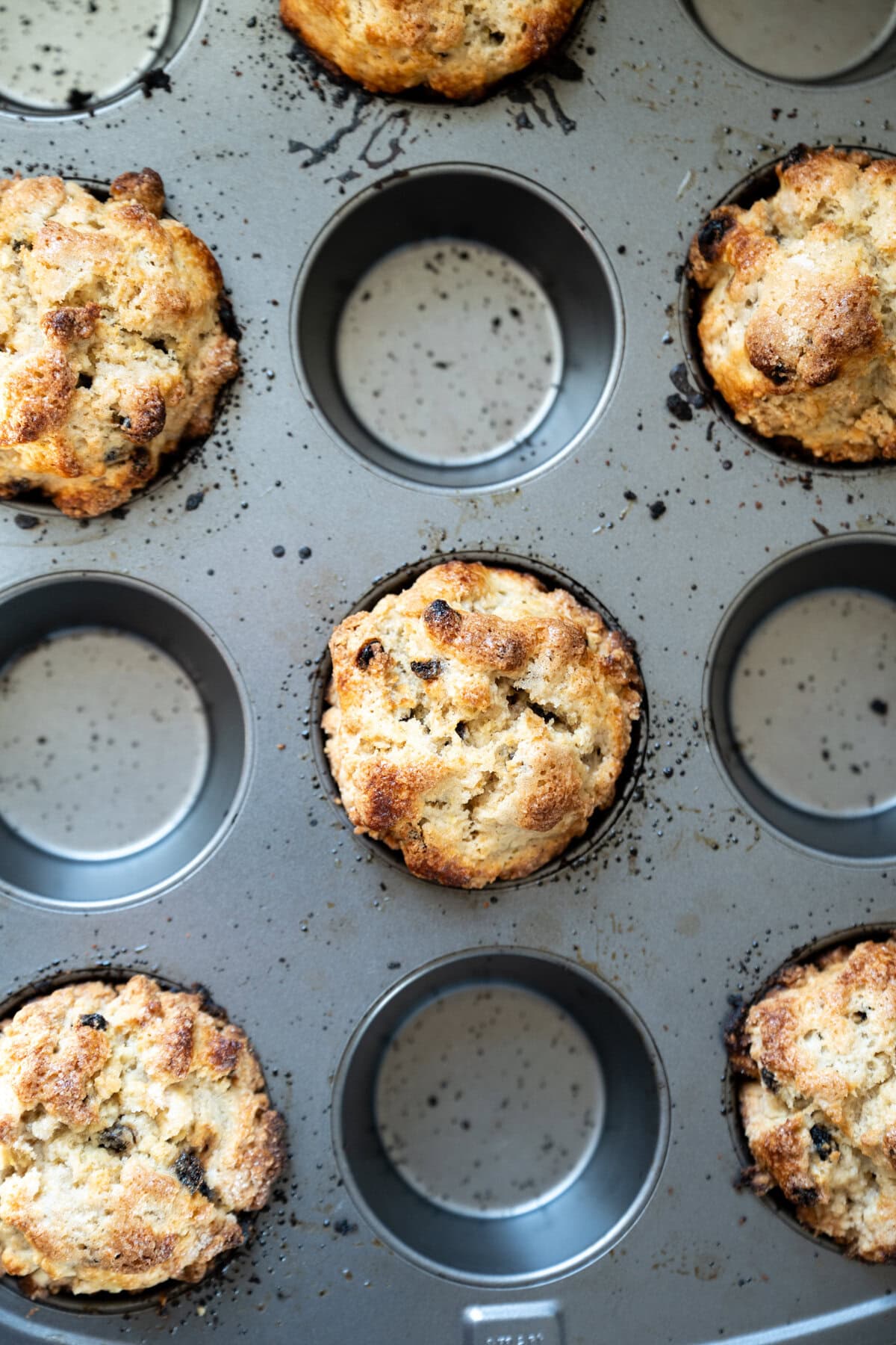 A muffin tin with several golden-brown, freshly baked Irish soda bread scones, some dotted with currants and a few compartments empty, viewed from above.