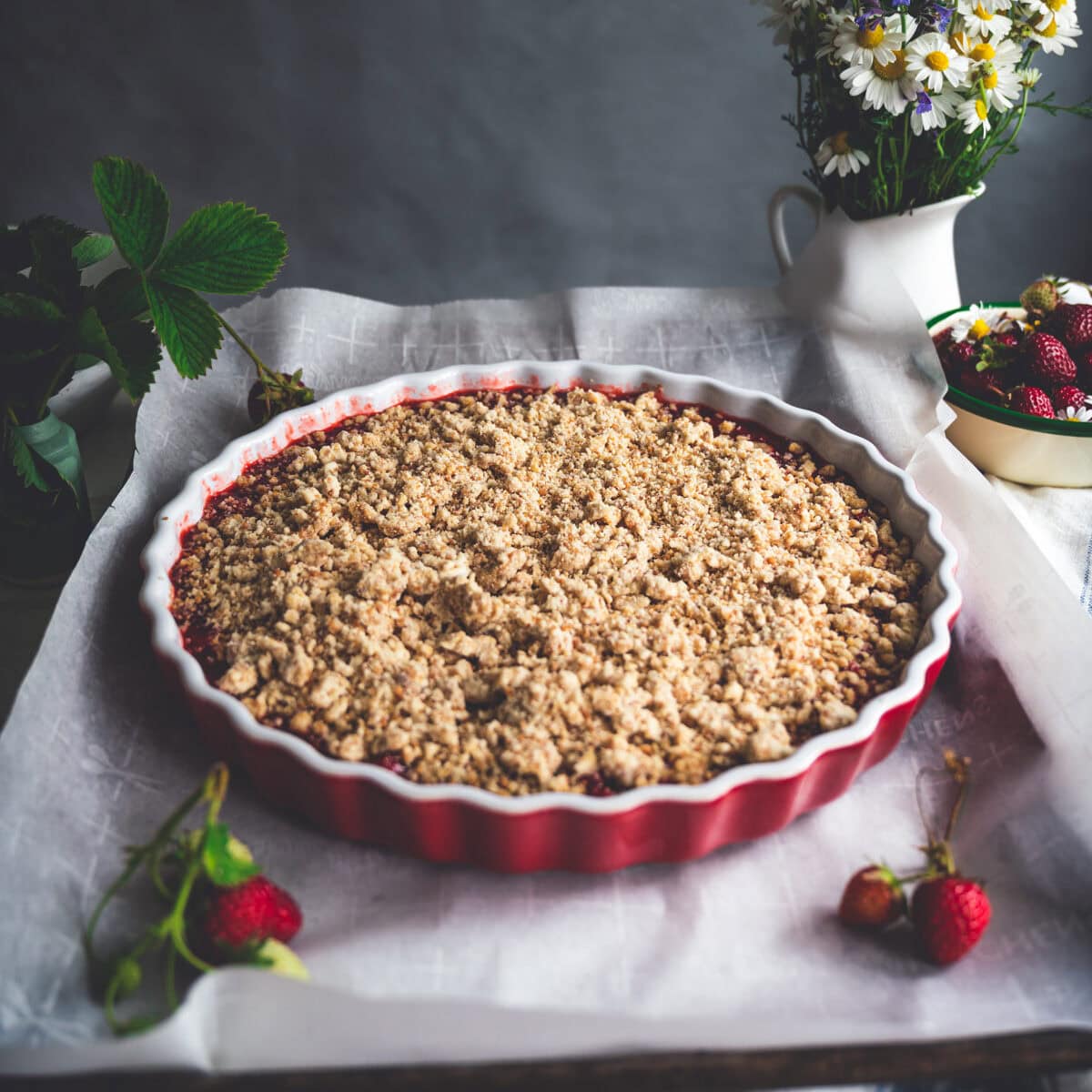 Uncooked strawberry rhubarb crumble assembled in a red fluted tart pan on a baking sheet lined with parchment paper.