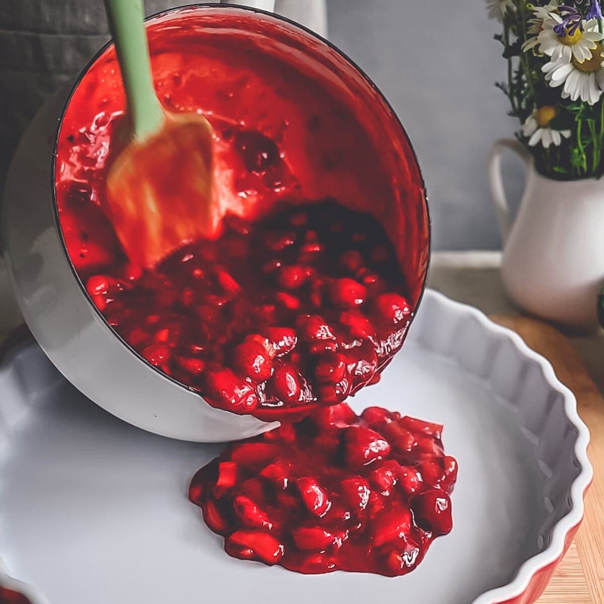 Pouring precooked strawberry rhubarb filling into a large fluted tart pan.