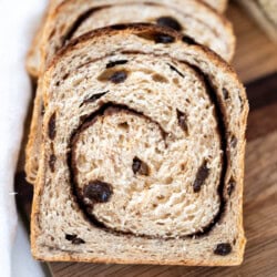 Sliced cinnamon raisin sourdough sandwich bread recipe on a wooden cutting board, showing a swirl of cinnamon and pieces of raisin in the soft, light brown bread.