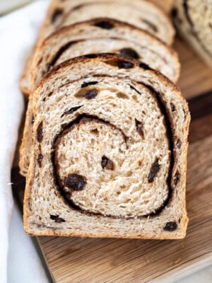 Sliced cinnamon raisin sourdough sandwich bread recipe on a wooden cutting board, showing a swirl of cinnamon and pieces of raisin in the soft, light brown bread.