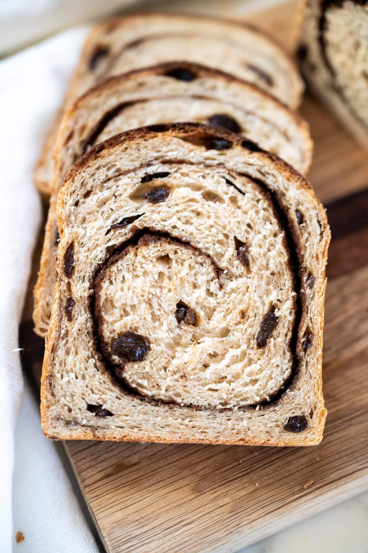 Sliced cinnamon raisin sourdough sandwich bread recipe on a wooden cutting board, showing a swirl of cinnamon and pieces of raisin in the soft, light brown bread.