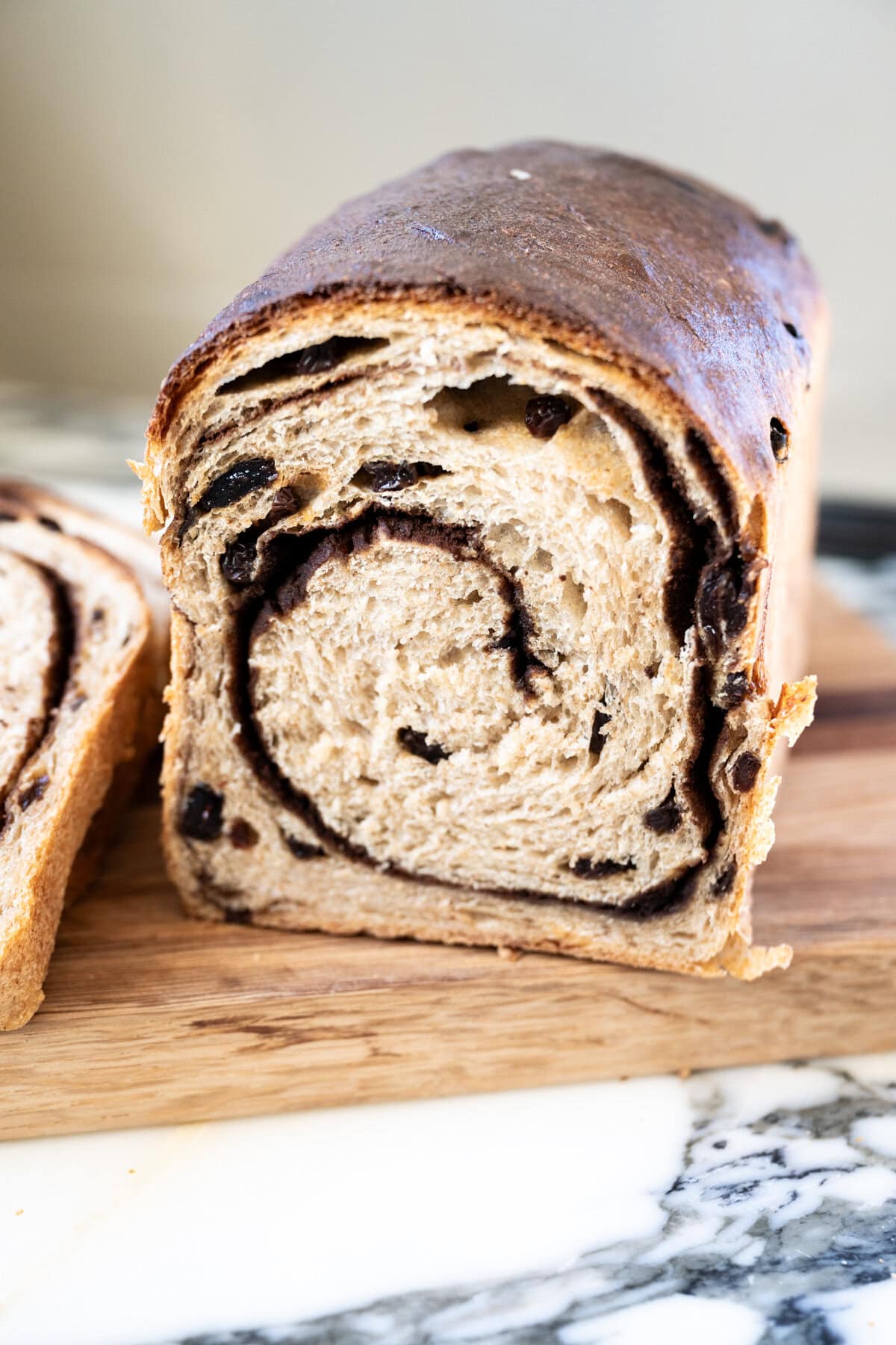 A loaf of soft sourdough cinnamon swirl bread with a dark spiral of cinnamon running through the sliced interior, resting on a wooden cutting board.