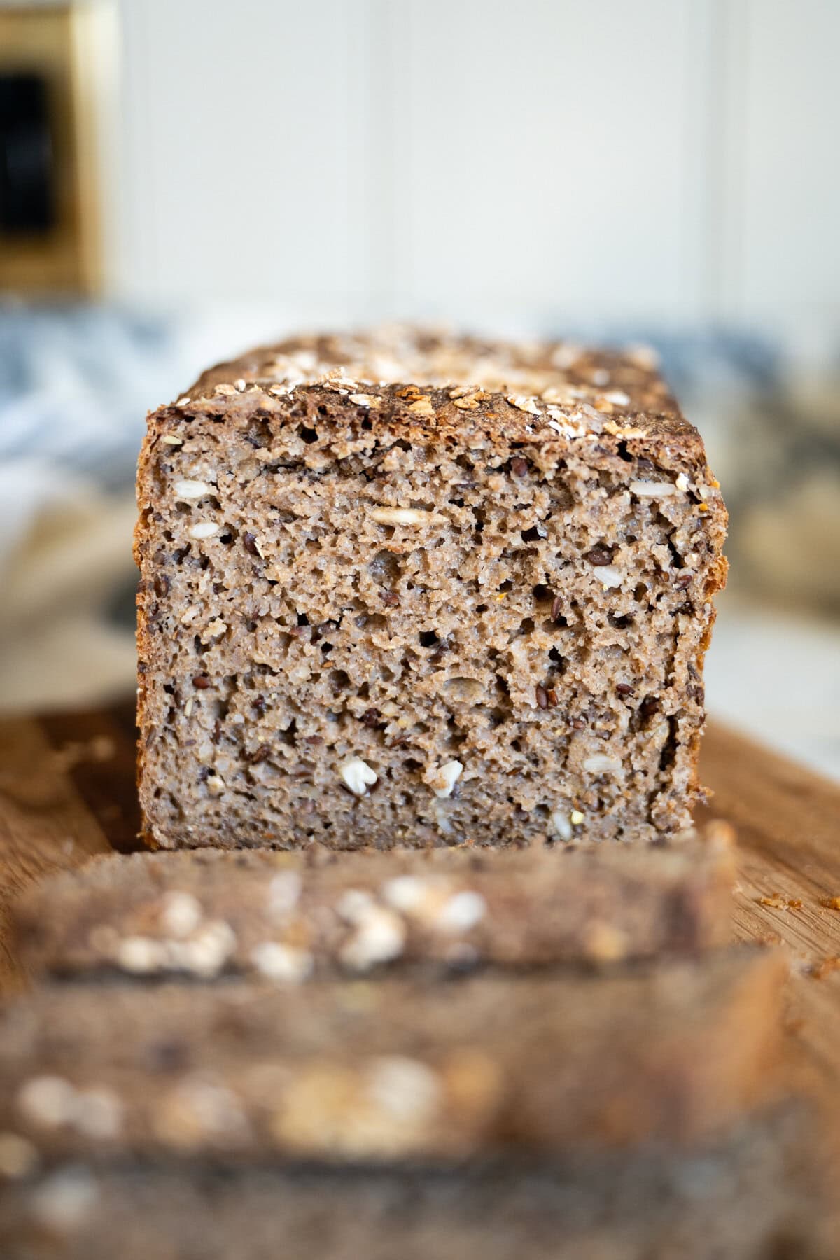 A close-up of seeded Danish rye bread showing dense moist texture and visible seeds, sitting on a wooden cutting board, with a few slices cut in the foreground.