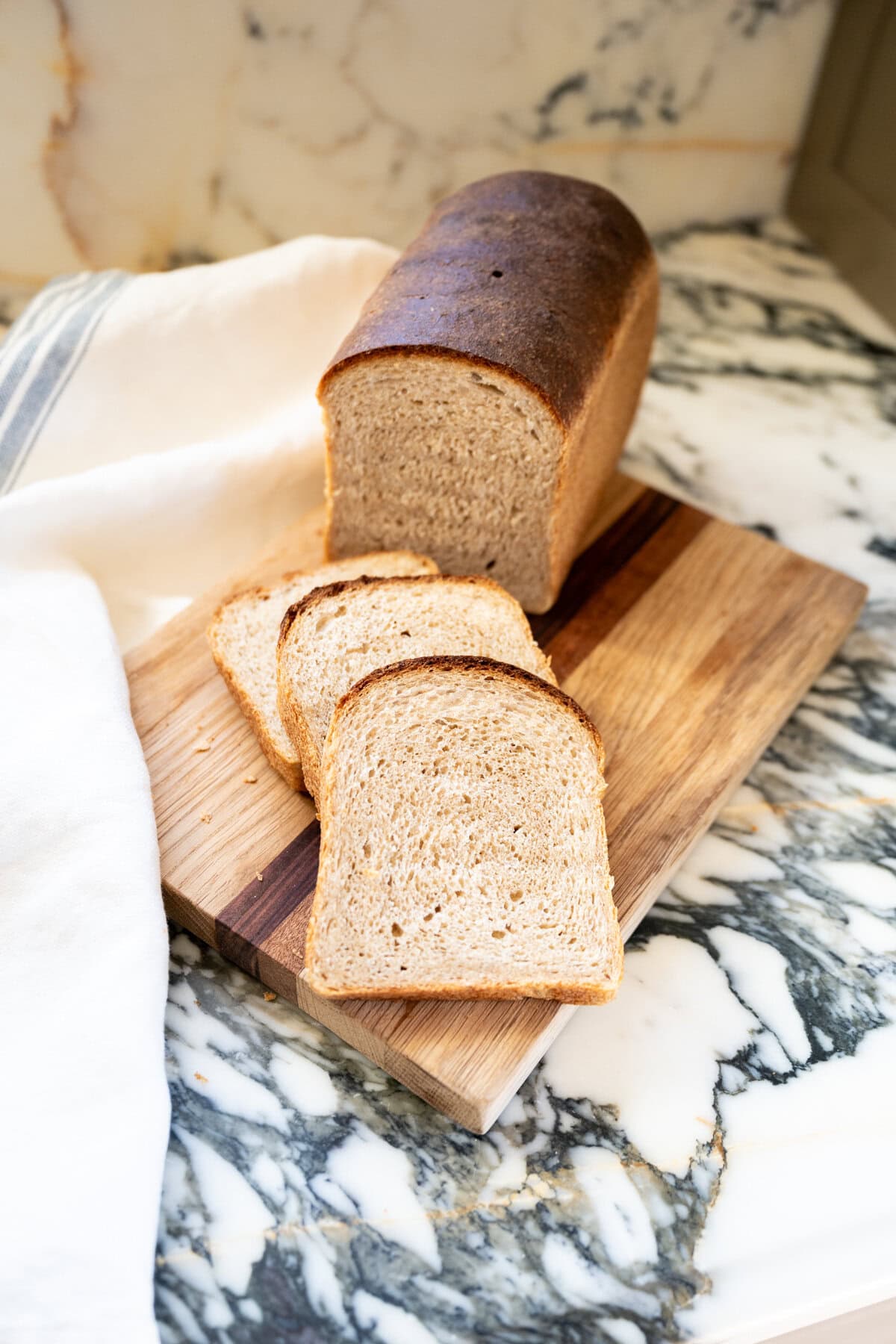 Fluffy slices of whole wheat sourdough sandwich bread stacked on a cutting board