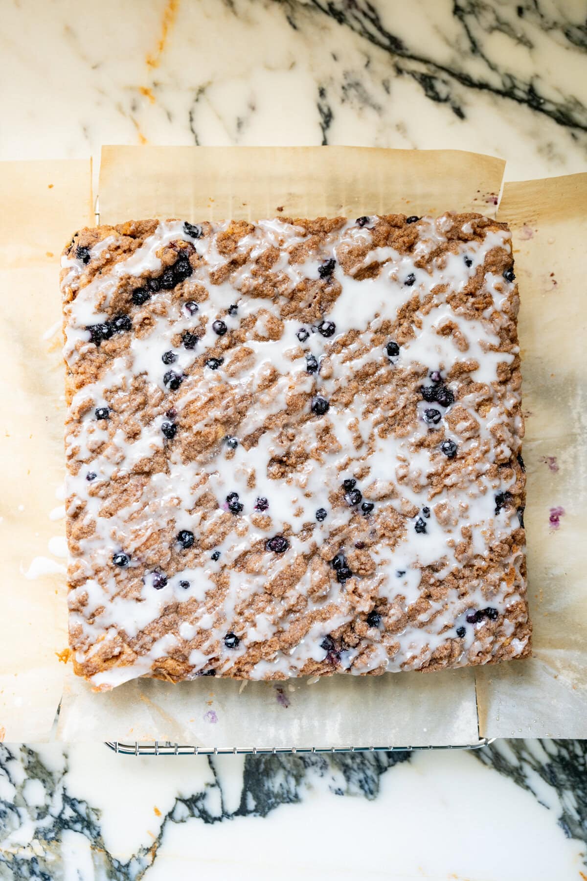 Homemade blueberry crumb cake topped with cinnamon streusel and a drizzle of lemon glaze, photographed from above.