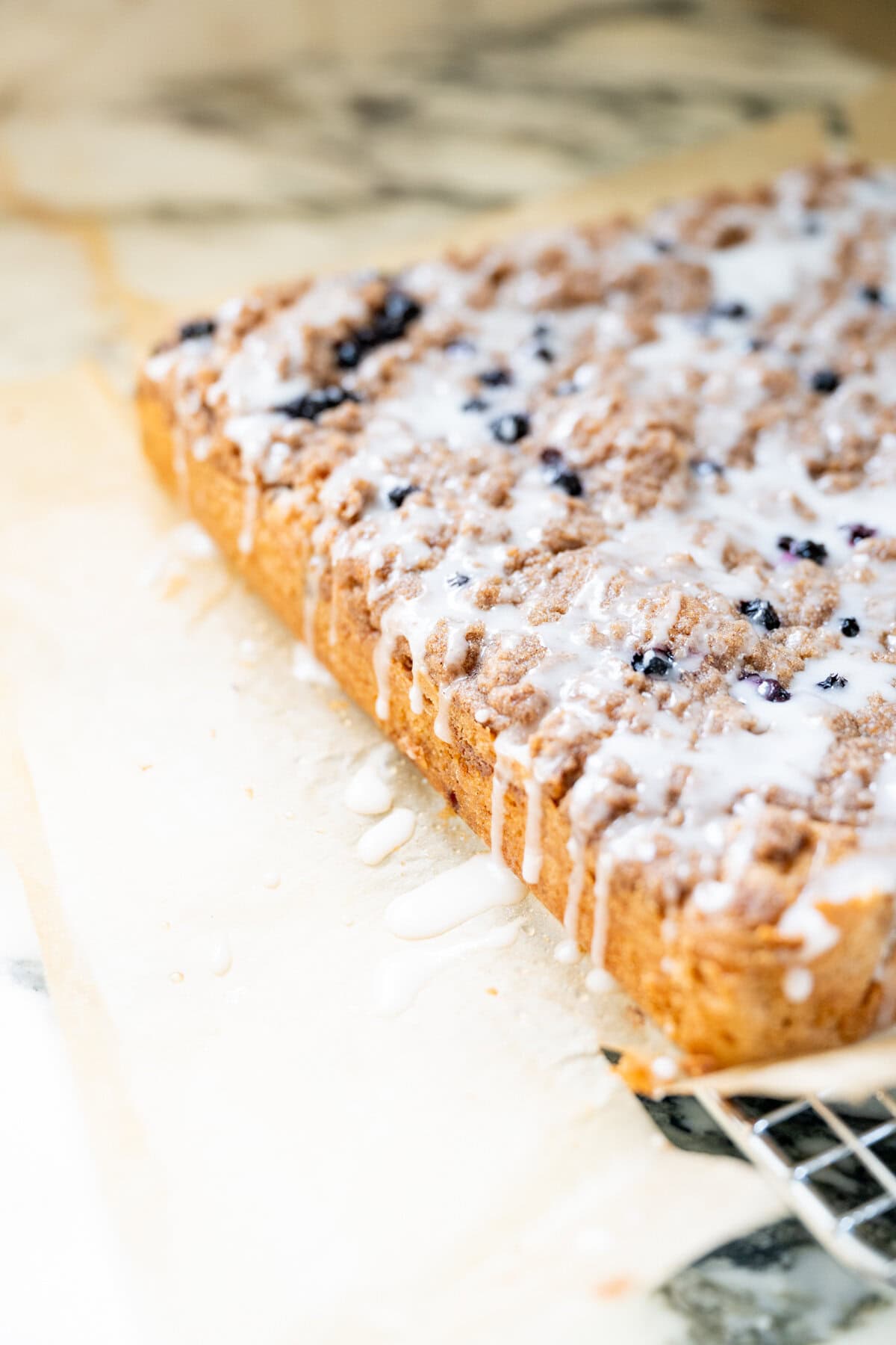 Side view of a homemade blueberry crumb cake with golden edges, a thick cinnamon streusel topping, and lemon glaze.