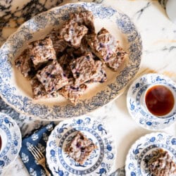 Blueberry crumb cake squares served with tea on vintage blue-and-white china beside a platter of cake.
