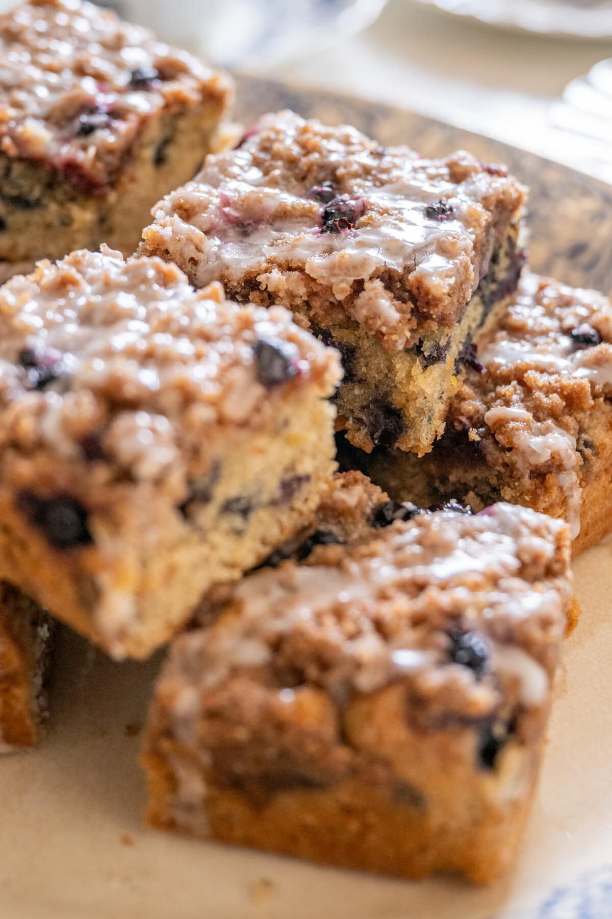 Close-up of thick blueberry crumb cake squares with a golden cinnamon topping, juicy blueberries, and lemon icing.