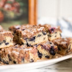 Thick squares of blueberry streusel cake stacked on a serving platter, with blueberries visible inside the cake.